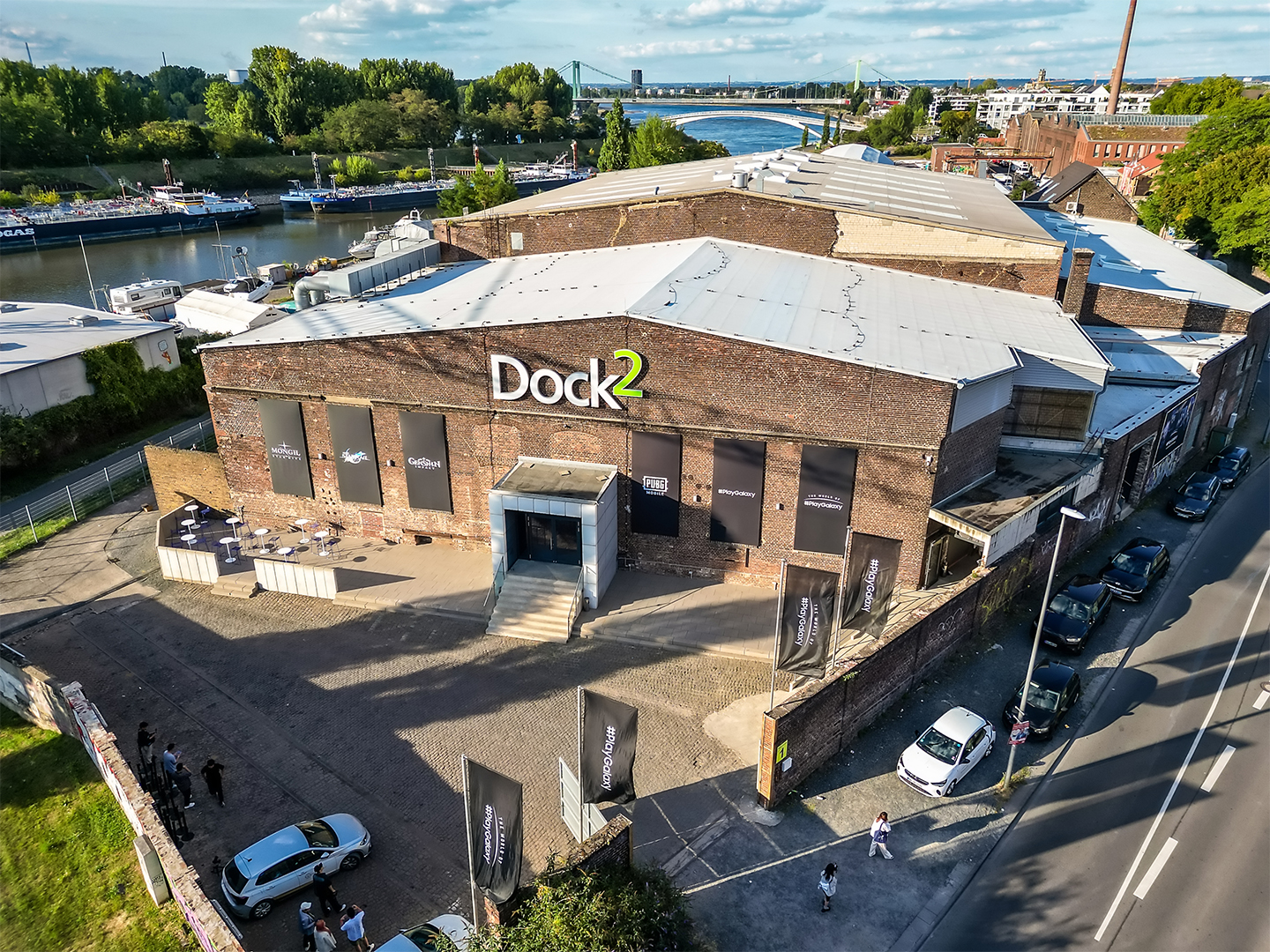 An aerial view of the exterior of a large building indicates some branding work done on the walls and entrance space in preparation for the Gamescom booth setup.