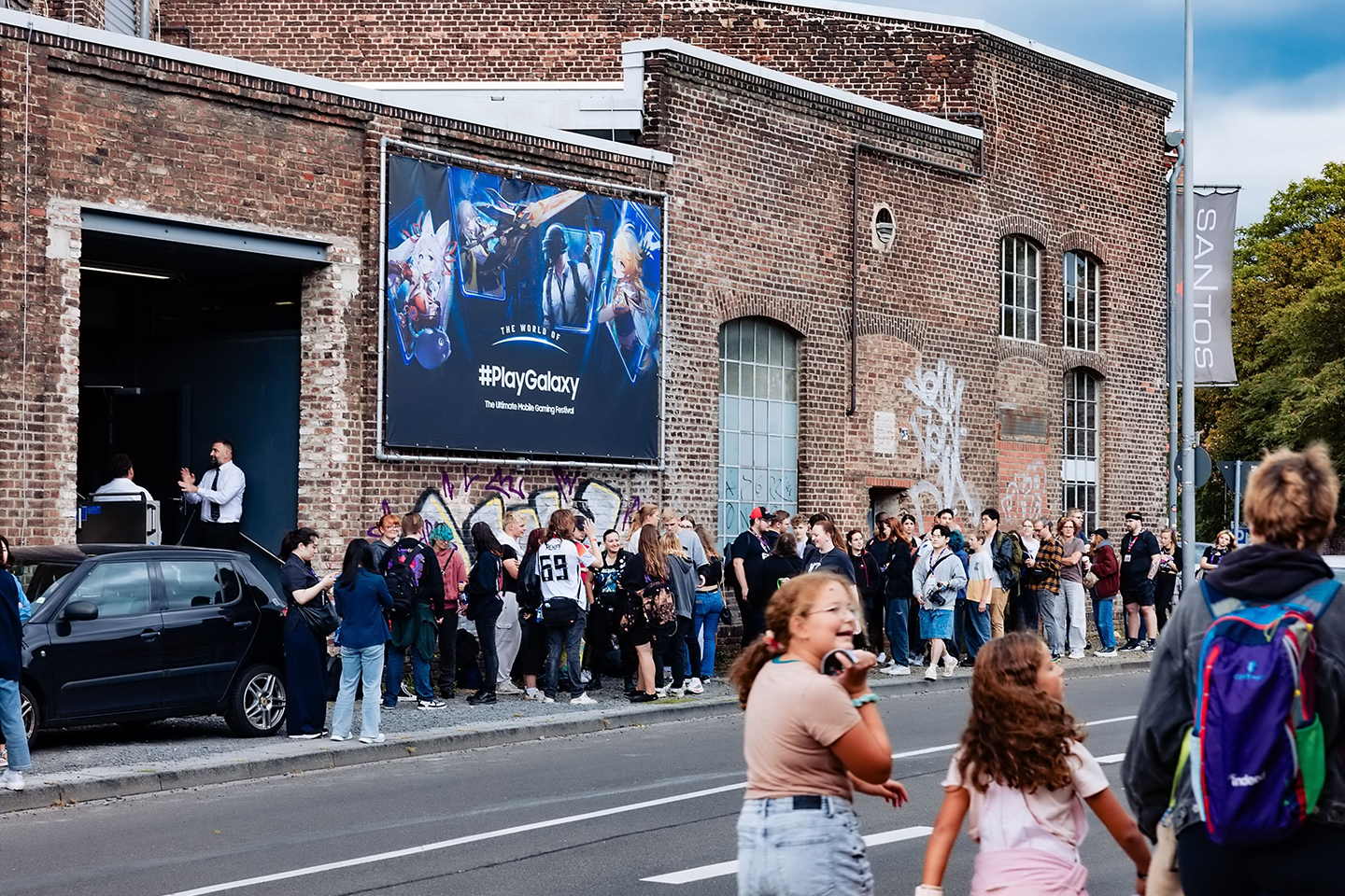 A crowd of people are waiting to enter a building featuring The World of PlayGalaxy banner.