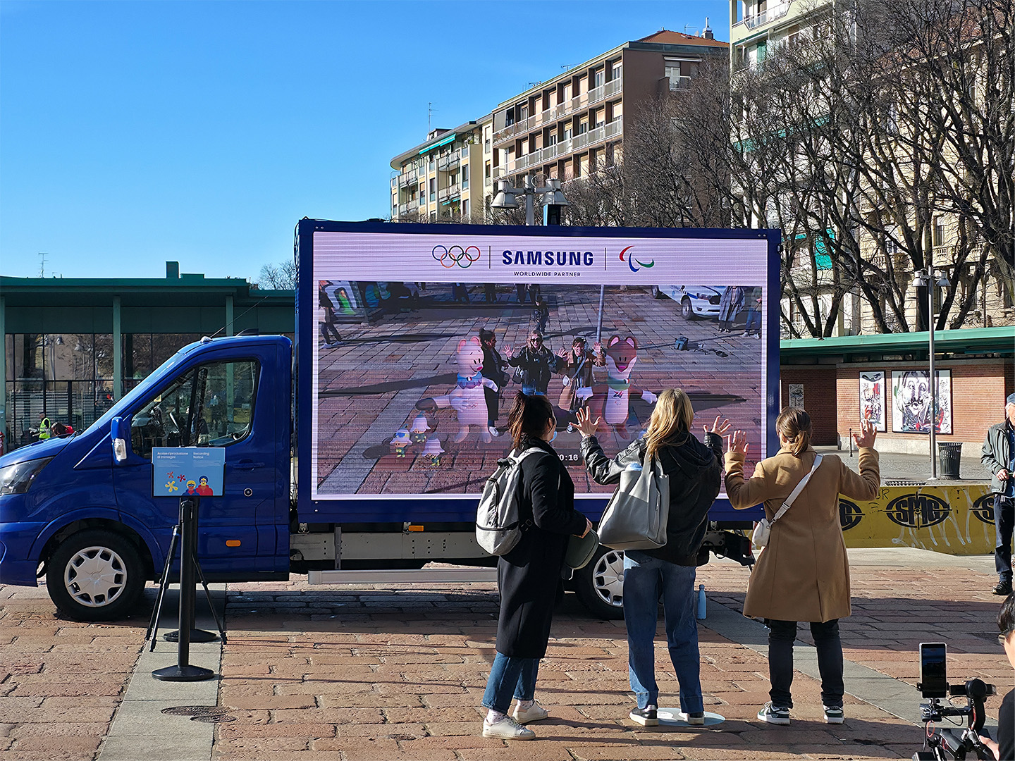 Three people in front of a Victory Truck take an AR photo with the Olympic mascots.