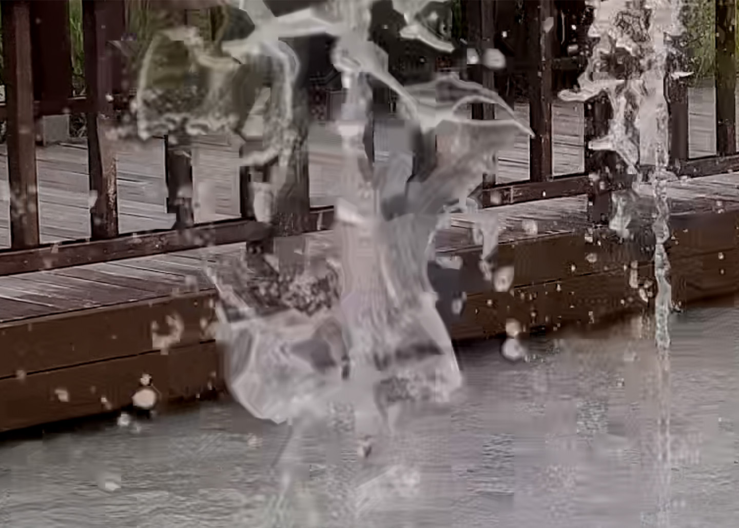 A still from a video of a splash of water in front of a boardwalk shows blurry small details like water droplets due to video file compression.