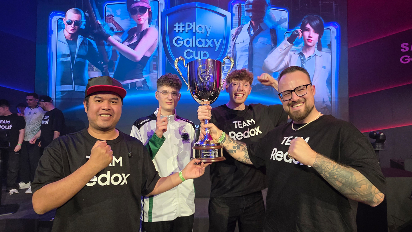 Four men are holding the PlayGalaxy Cup against a digital backdrop featuring the tournament's name and game characters.